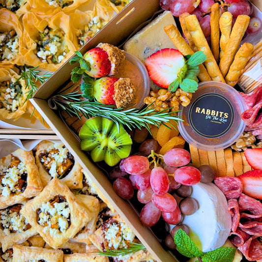 A variety of gourmet snacks and appetizers arranged on trays, including mini quiches, pastries, and cheese balls, indicative of corporate catering options.